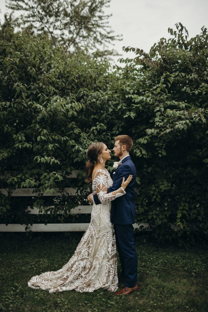 Couple portraits with groom in navy suit against greenery wall