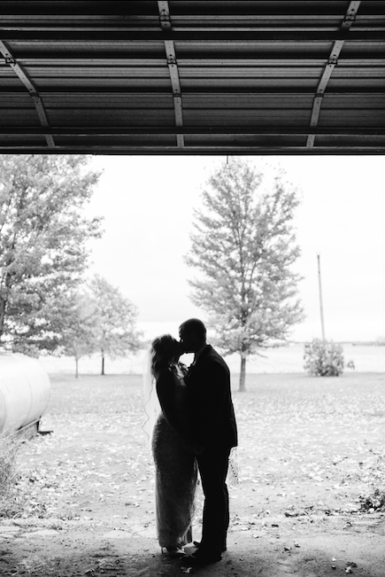 Black and white picture of couple outside their barn on their wedding day.